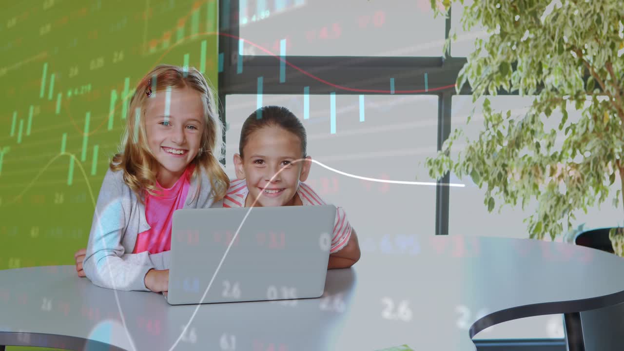 Two girls typing on silver laptop, starting finance charts overlay across classroom for lesson