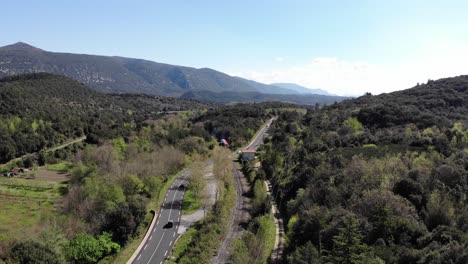 Aerial:-red-and-white-old-train-among-vineyards-and-green-fields-by-a-road-with-light-traffic-in-southern-France