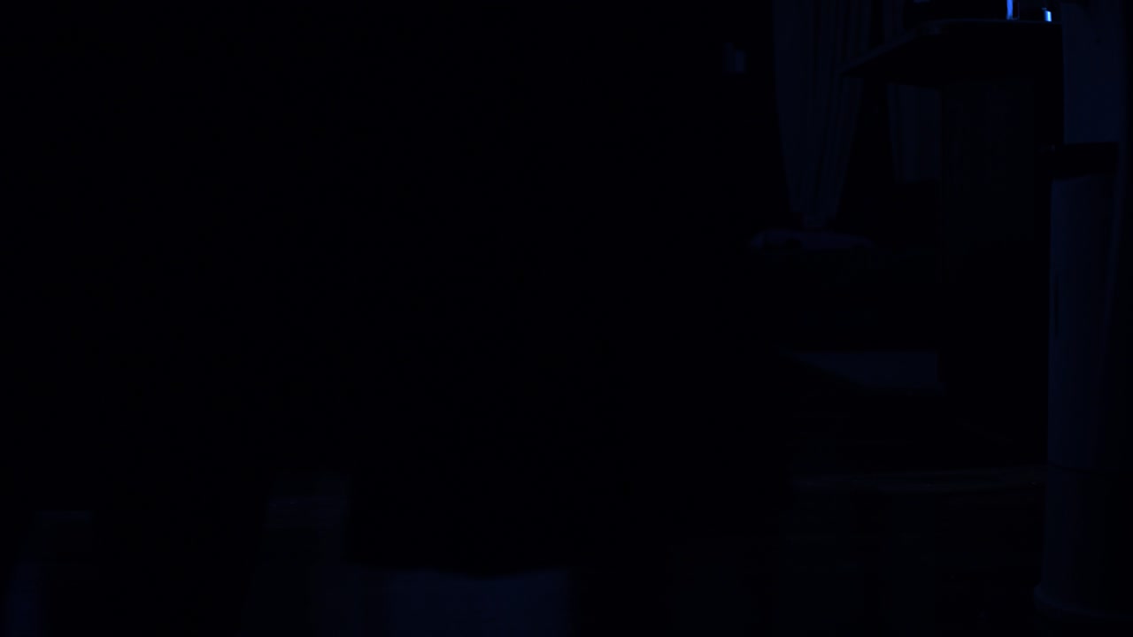 una figura oscura y encapuchada pasa junto a la cámara hacia una fuente de luz que se derrama desde una habitación oculta en la oscuridad de la noche en una casa fría