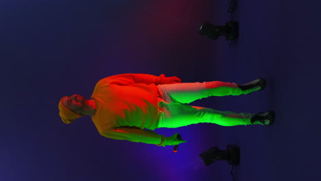 vertical video. a man in a yellow jacket dancing on a blue background. the singer in the studio in the neon light dancing and singing. changing the background color. strobe lights and funny dancer