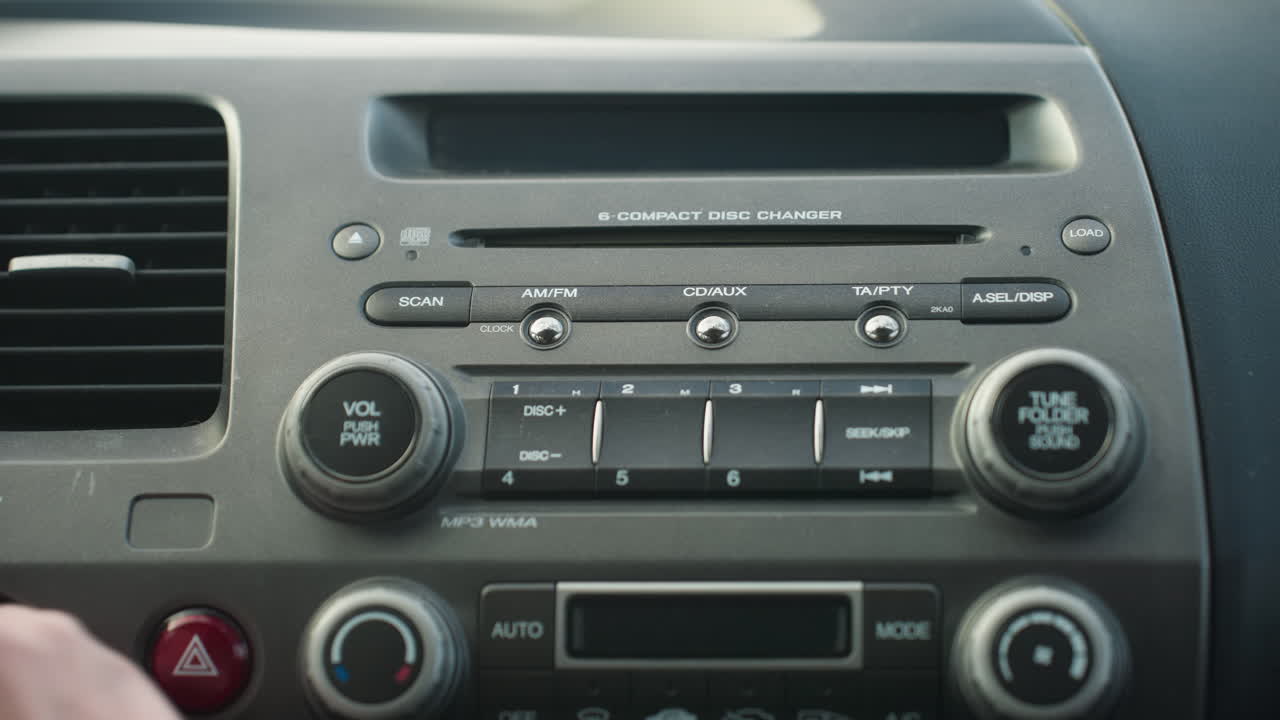 close up of car dashboard showing digital display with CD track information while driver turns off car, focus on stereo controls and buttons with clear text and lighting on panel visible