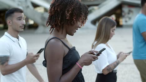 Cheerful-African-American-lady-using-smartphone-during-stroll