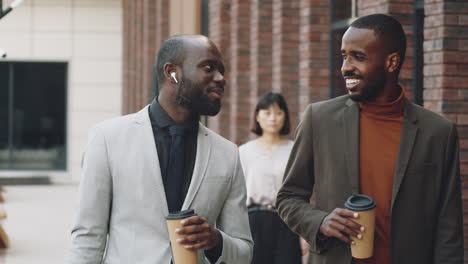 Two-Black-Businessmen-Chatting-and-Walking-on-Street-with-Coffee