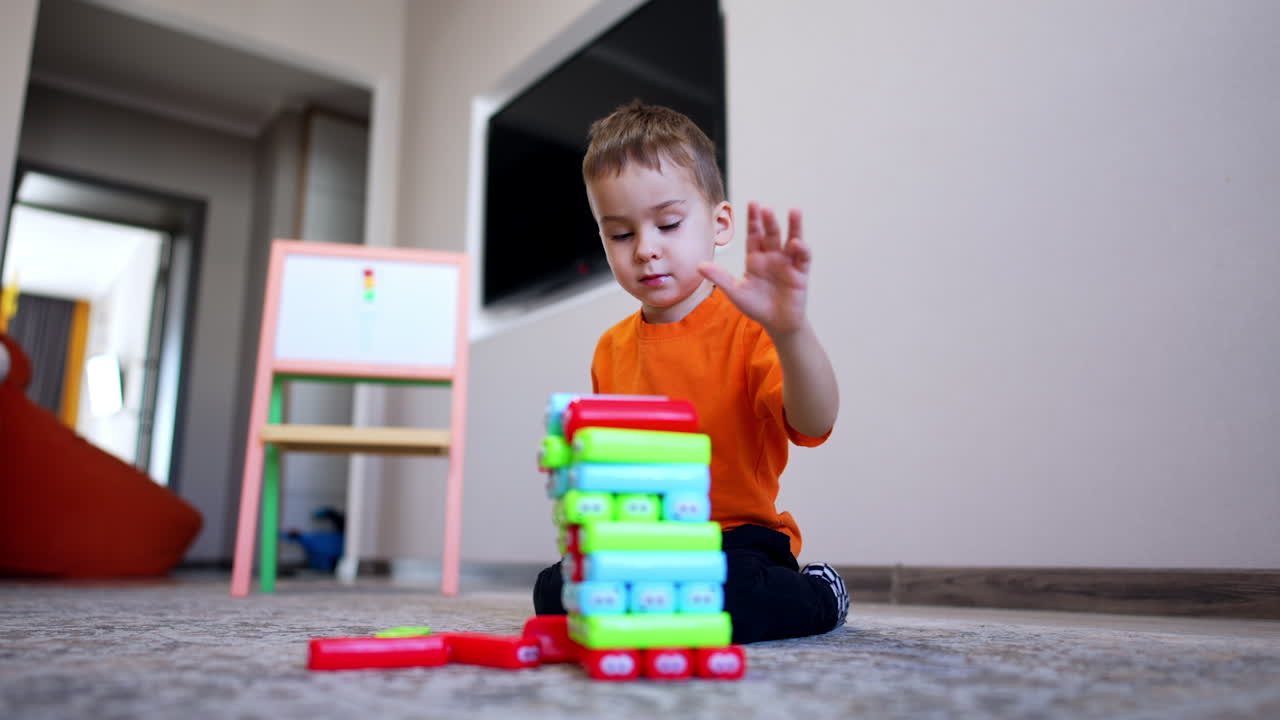 Lovely baby boy builds a tower of colorful blocks. Cute toddler kid plays on the floor at home. Low angle view.