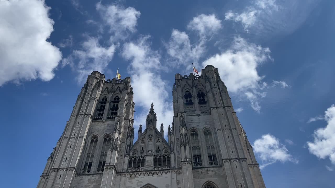 Vista de ángulo bajo de las torres gemelas de la catedral de San Miguel y Santa Gúdula elevándose contra el cielo azul con nubes dispersas en Bruselas. Arquitectura gótica de piedra e imagen de un monumento religioso histórico