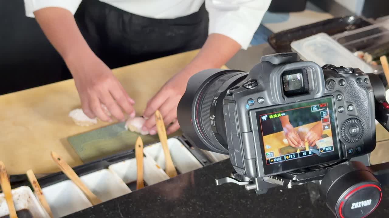 Chef profesional prepara sushi en la barra mientras una cámara digital graba un primer plano en una luminosa cocina de restaurante