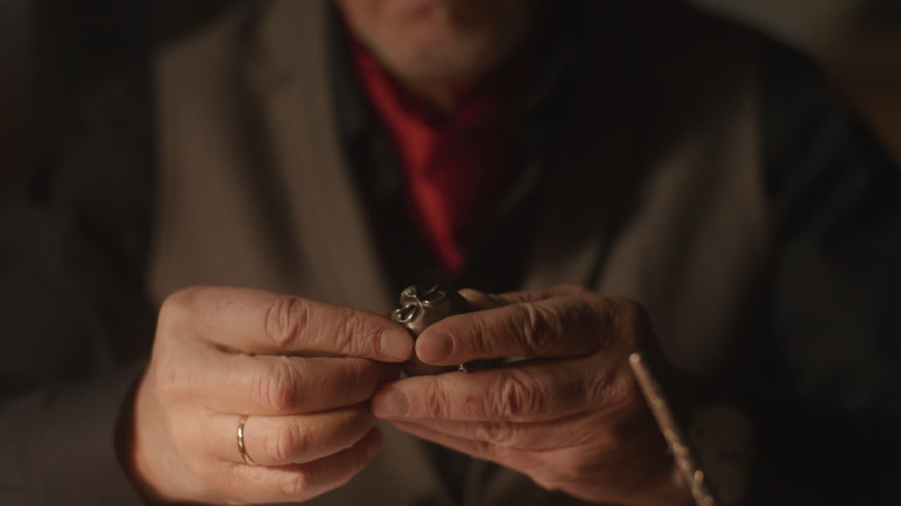 Older passionate man evaluates an old silver skull watch in his office at night