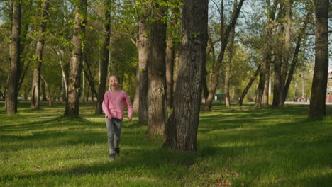 una niña sonriente salta y corre a lo largo de la hierba exuberante en el parque