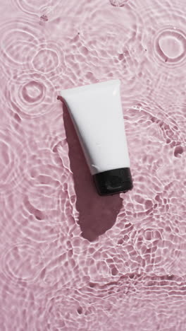 vertical video of beauty product tube in water with copy space on pink background