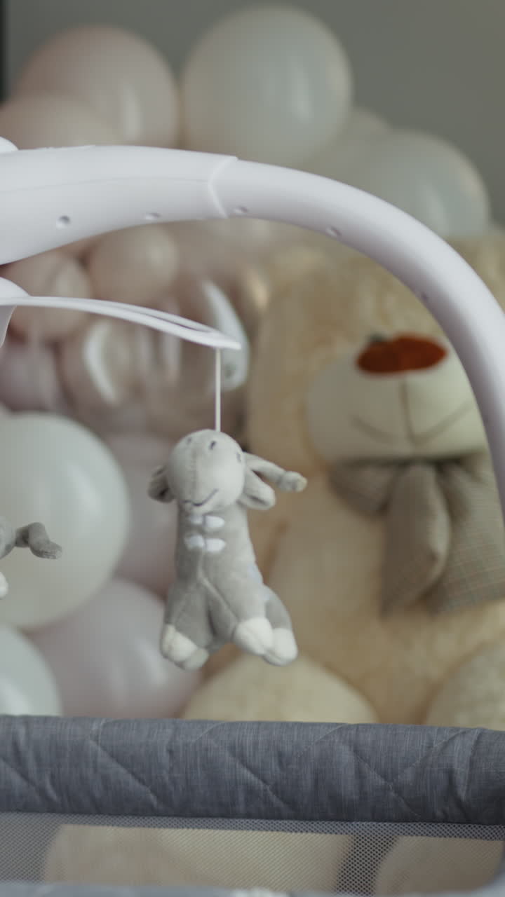 Primo piano di una giostrina per culla con giocattoli di peluche appesi sopra un grande orsetto e colori pastello.