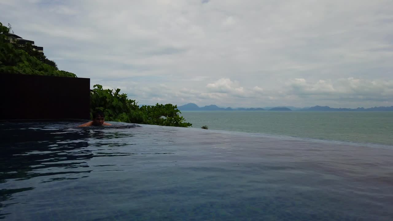 Asiatischer Mann schwimmt in einem Pool mit Blick auf den wunderschönen Ozean