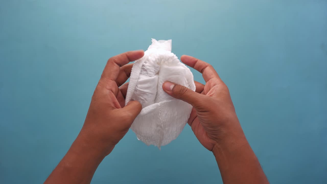 primer plano de manos sosteniendo un pañal blanco para bebés
