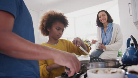 padres afroamericanos y su hija preadolescente preparando comida juntos en la cocina, de cerca