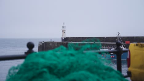 looking over fishing nets in the foreground to the lighthouse in mevagissey harbour, cornwal, england, uk