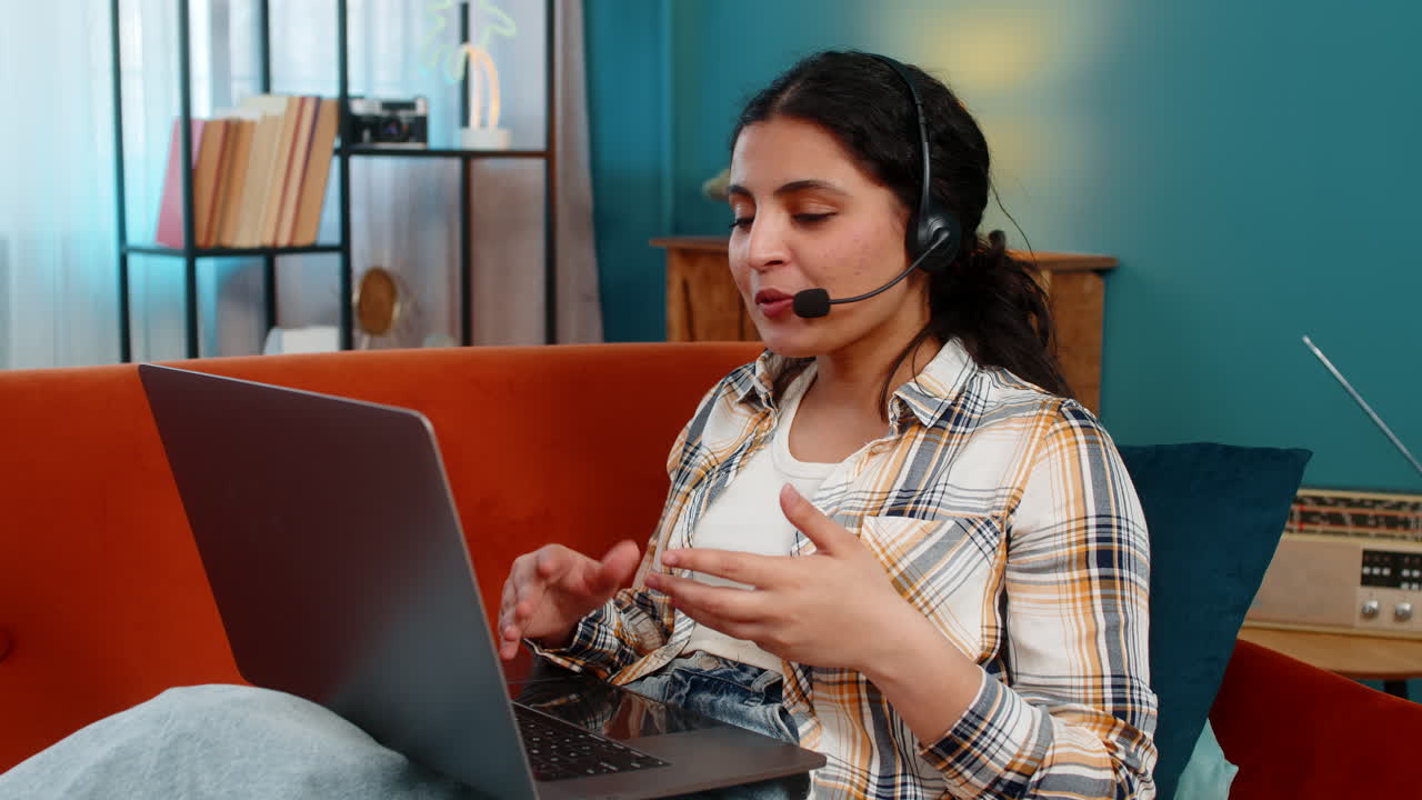 Operatrice di call center indiana che lavora a casa con un portatile e un microfono concentrato