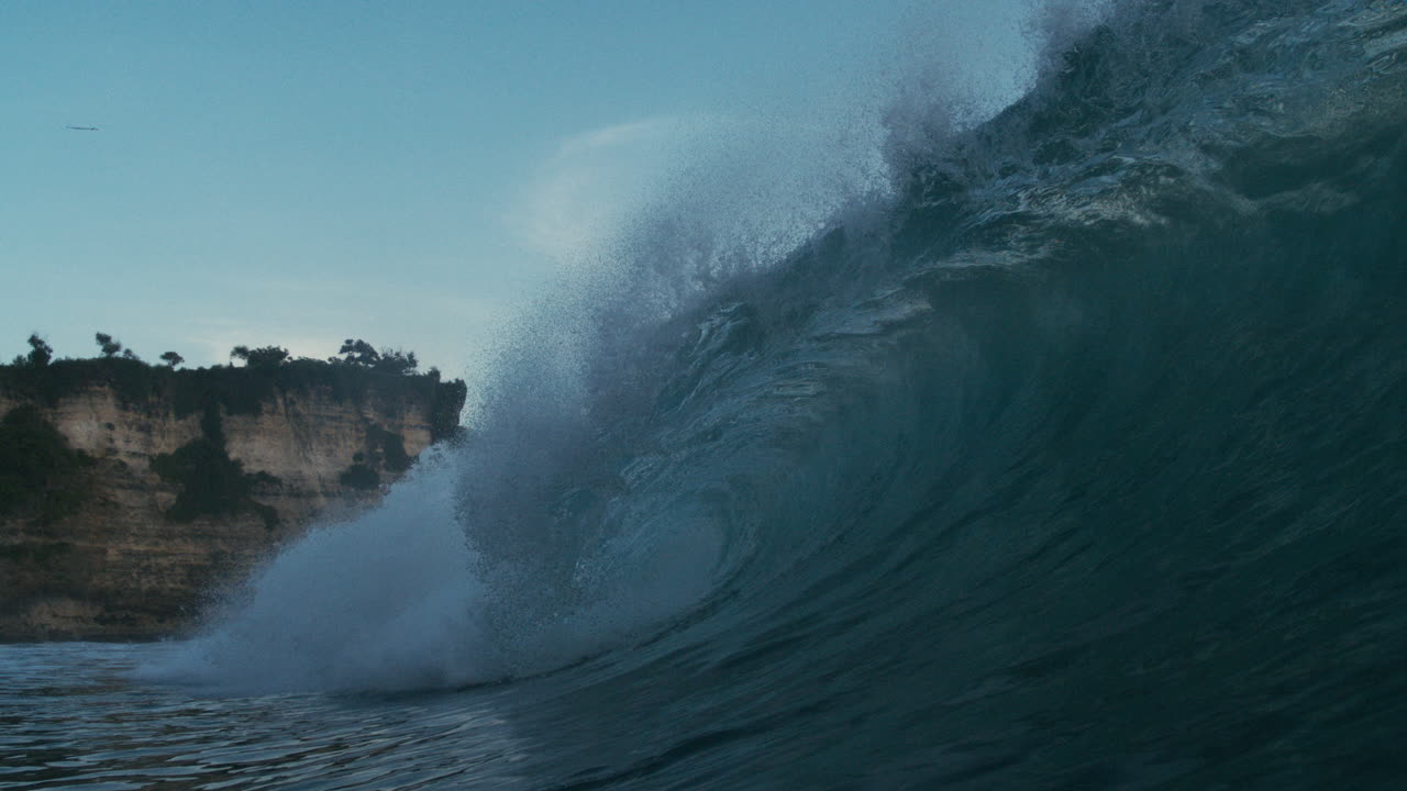 Large wave crashes near rocky point in tropical setting with vibrant slow textured motion