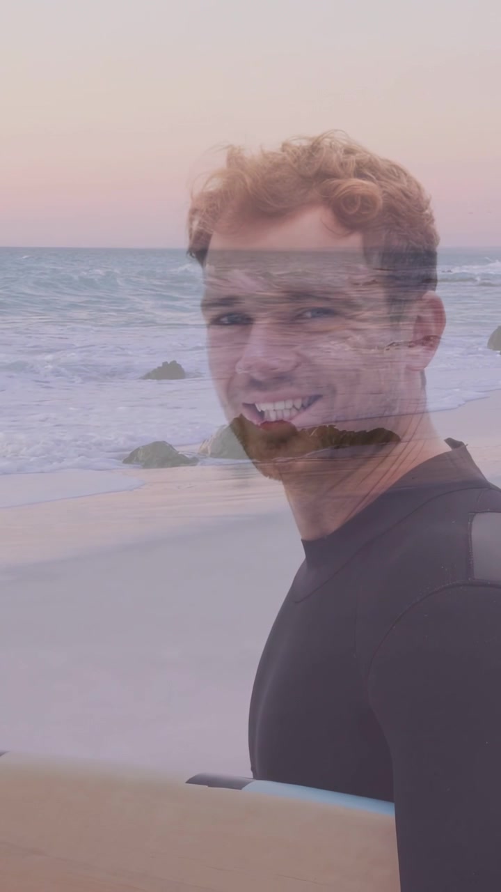 Vertikales Video: Surfer geht am Meer entlang auf Kamerasignal, dreht sich um, lächelt, Surfbrett mit Logo als Werbefläche.