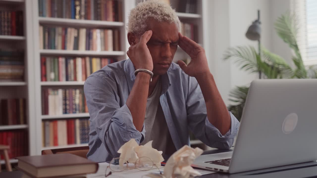 Stressing african man with pain suffering from migraine rubbing his temples