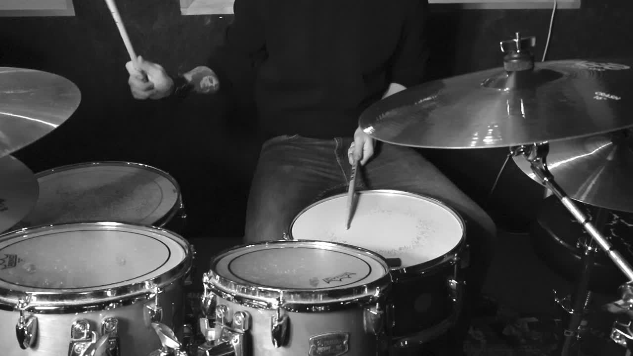 Slow motion grayscale footage of a person or a man with tattoos playing acoustic musical instrument drums and hitting them with drumsticks. cymbals are moving after hitting them in a funny way.