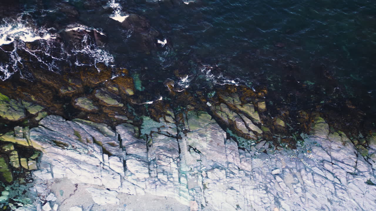 Drone top down pan as ocean waves crash on rocky shoreline of Newport Rhode Island