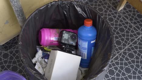 A-damaged-GoPro-camera-is-discarded-in-a-black-plastic-trash-bag,-placed-in-a-trash-bin