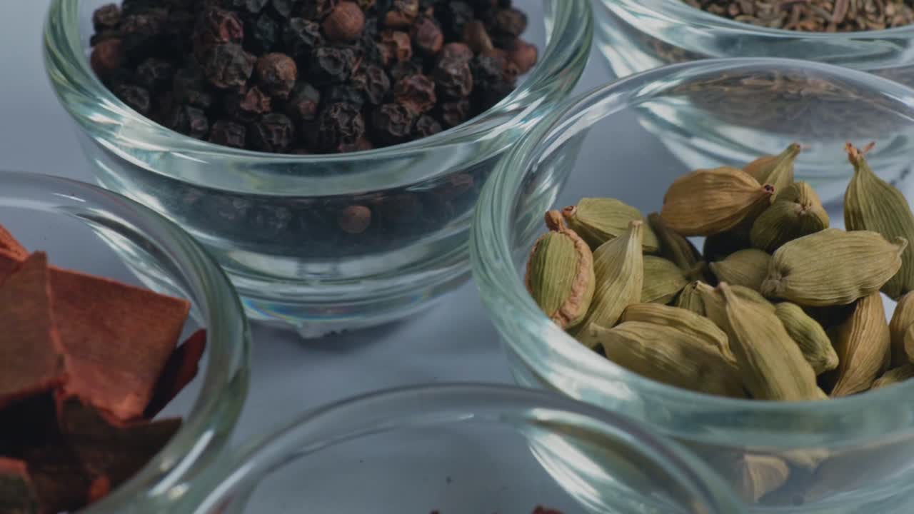 different types of whole spices Shahjeera, Kali mirch, Choti elaichi, Dalchini, Laung and Sukhi lal mirch in small glass bowl, 4k, push back shot