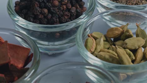 different types of whole spices shahjeera, kali mirch, choti elaichi, dalchini, laung and sukhi lal mirch in small glass bowl, 4k, push back shot