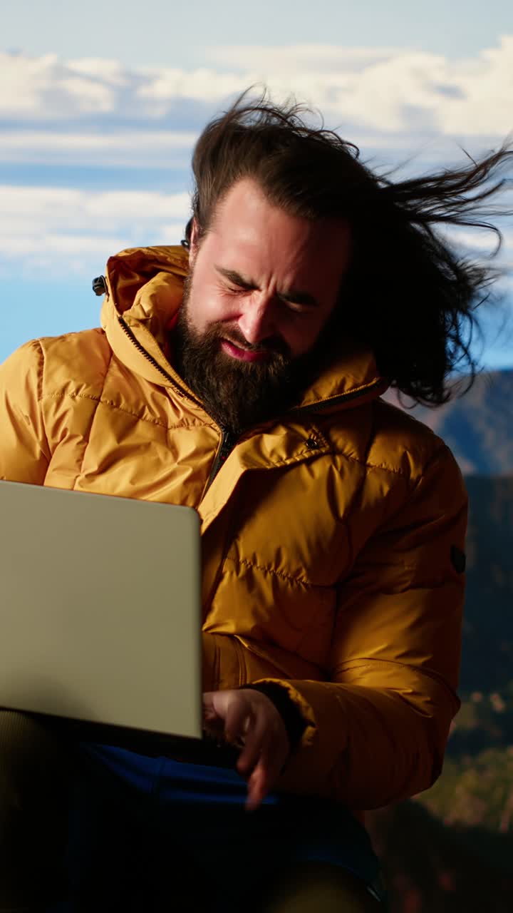 Uomo barbuto che ride mentre lavora al laptop all'aperto in montagna.