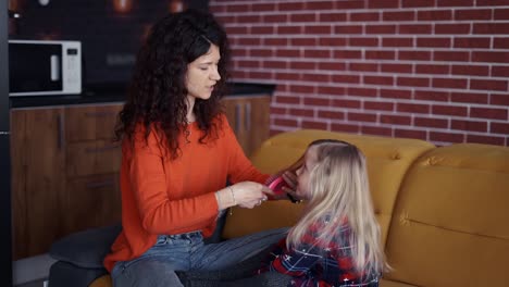 mamá está peinando el cabello de la hija en la sala de estar