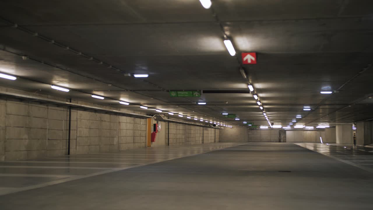 A cinematic slow motion shot capturing the quiet ambiance of an empty parking garage illuminated by overhead lights