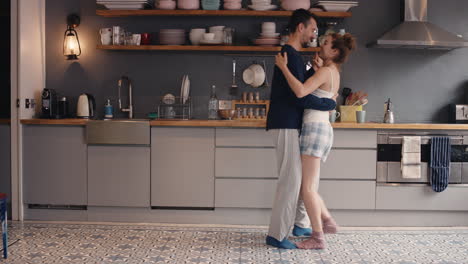 Feliz-Pareja-Joven-Recién-Casada-Bailando-Escuchando-Música-En-La-Cocina-Usando-Pijamas-Por-La-Mañana-En-Casa