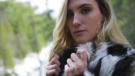 confident young woman wearing a fur jacket poses for the camera in a winter forest setting