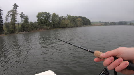 A-fisherman-reels-on-a-Swiss-lake,-Vaud-during-a-cloudy-day-in-autumn