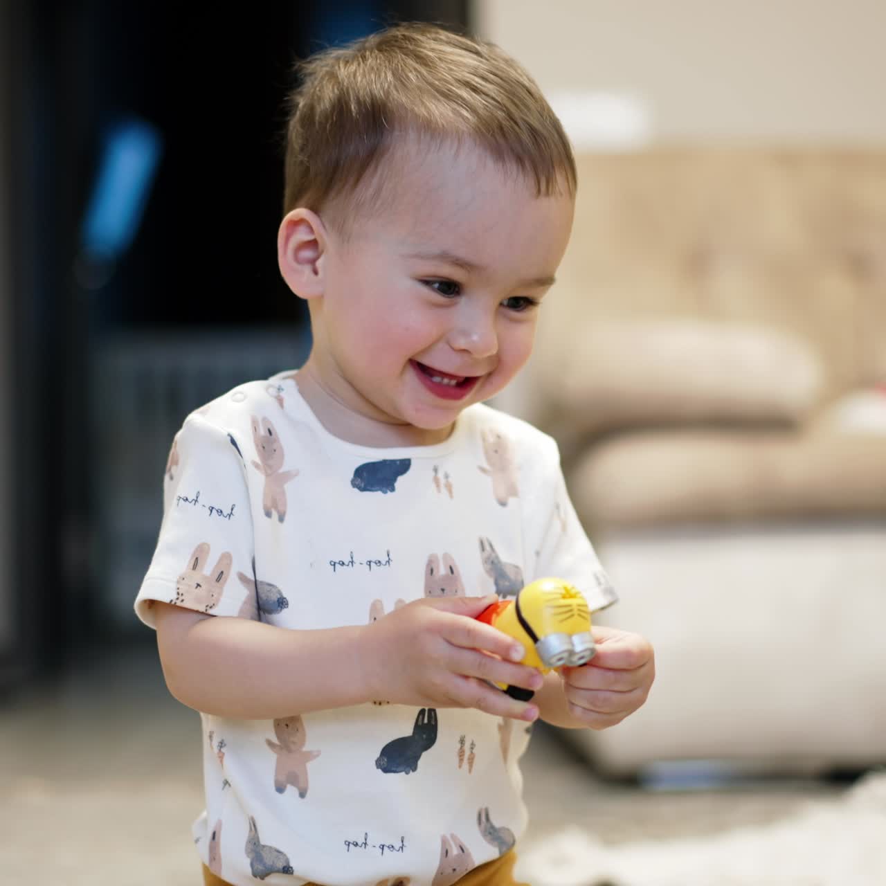 Un neonato sorridente e bellissimo tiene in mano un giocattolo. Il bambino gioca con un giocattolo esultando gioiosamente. Sfondo sfocato