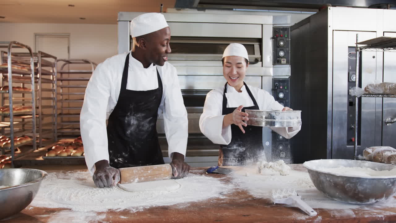Blije bakkers van verschillende achtergronden werken in een bakkerijkeuken, deeg uitrollend, slow motion