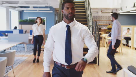 businessman walking through modern office checking data on smart watch