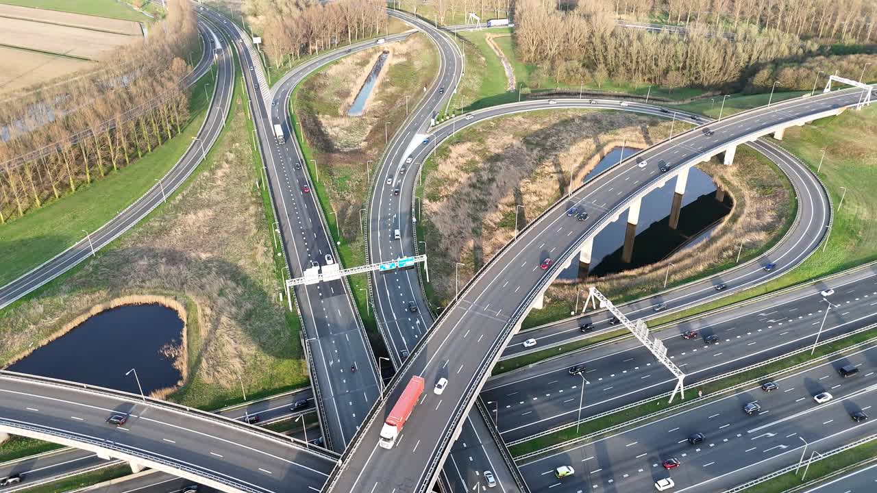 Dynamic aerial footage of Ridderkerk's intricate highway interchange in the Netherlands. The shot captures vehicles navigating the complex overpass network under clear daylight