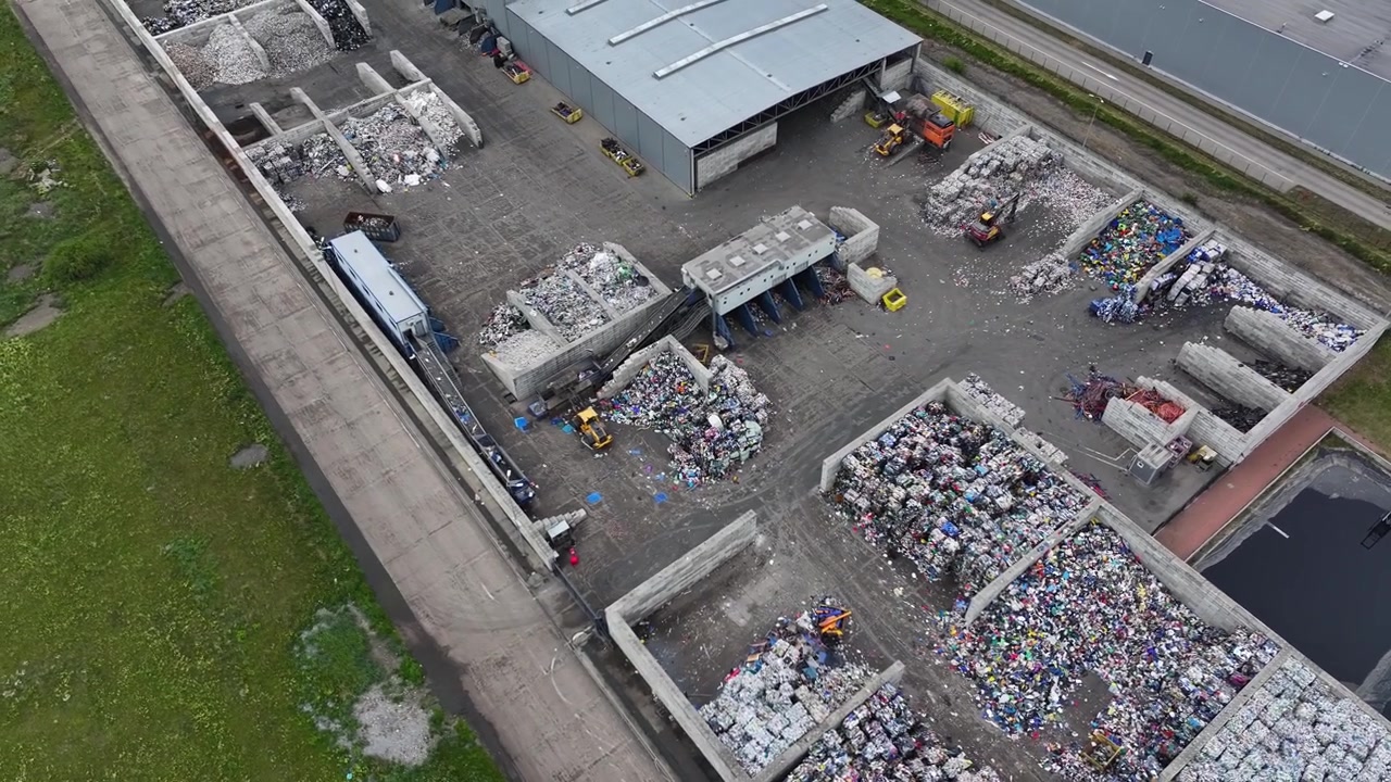リサイクル施設でプラスチック廃棄物が分別・処理される。産業機器が材料の回収と分離に使用され、トラックがリサイクル可能な材料を敷地内で輸送する。