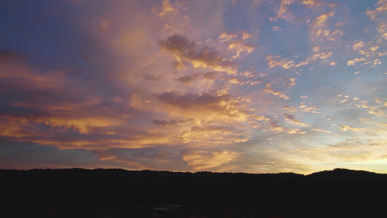 Un amanecer tranquilo se despliega, con suaves tonos rosados y azules iluminando el cielo. Nubes tenues brillan suavemente, enmarcando un horizonte pacífico capturado bellamente por un dron.