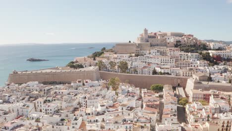 aerial view of ibiza city, the old town and the city walls of eivissa, in the island of ibiza, on a sunny and clear day, just after sunrise, with birds flying alongside the city wall