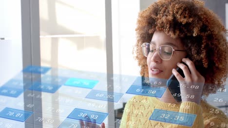 Data-processing-on-interface-over-biracial-casual-businesswoman-talking-on-smartphone-at-office