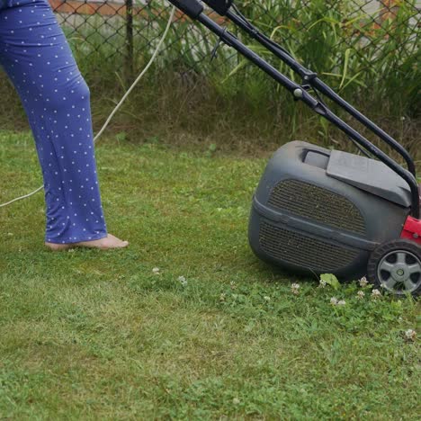 mowing a lawn with an electric mower. legs of young woman mowing lawn by lawn mower near country house