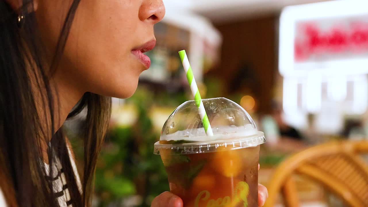 A woman sips an iced drink through a straw in a vibrant Gold Coast cafe setting, captured in natural lighting