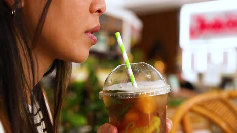 a woman sips an iced drink through a straw in a vibrant gold coast cafe setting, captured in natural lighting