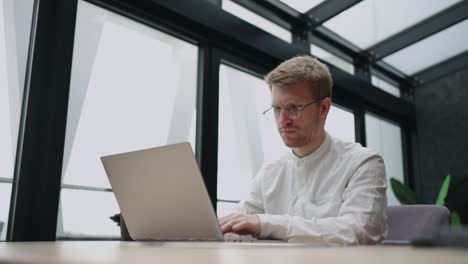 handsome man is working with laptop in modern office in daytime, person in white shirt is surfing internet