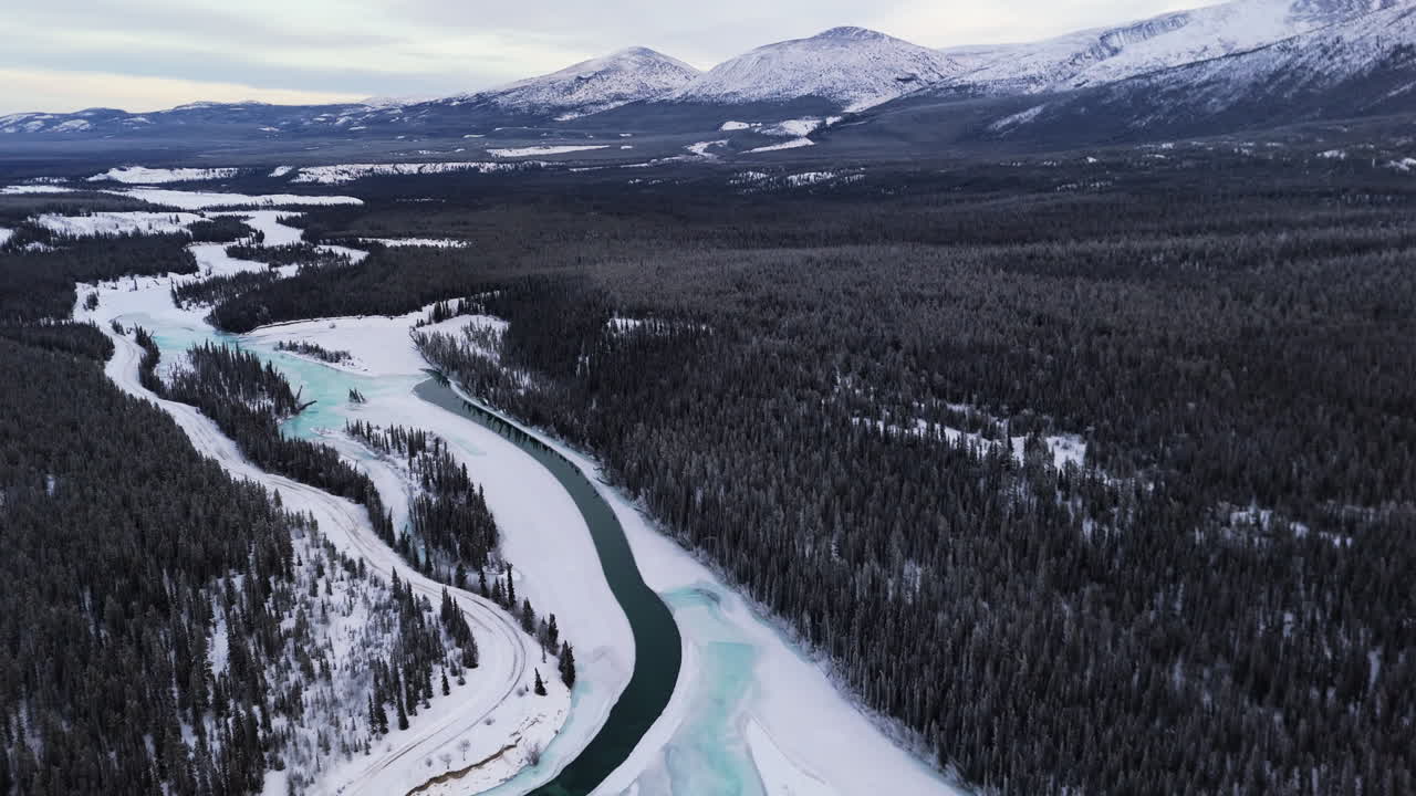 The Takhini River Flowing Through a Winter Landscape, Framed by Dense Forest and Snow-covered Mountains in Yukon, Canada - Aerial Drone Shot