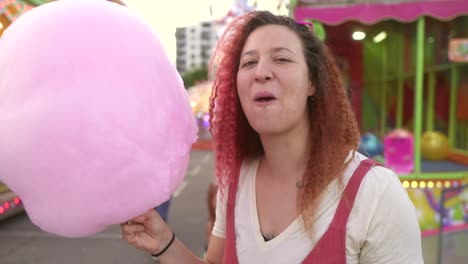mujer feliz con el cabello rojo comiendo azúcar de algodón en la feria