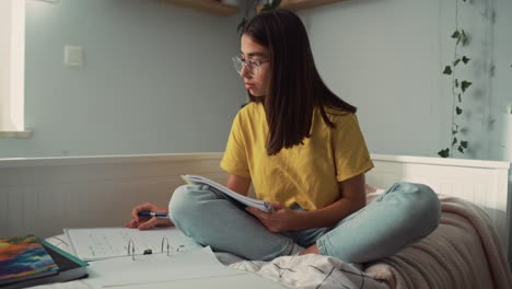 caucasian teenage girl sitting on bed and doing homework