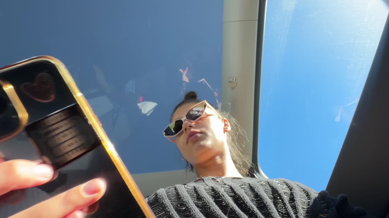 Woman looking up at sky from car sunroof while using phone
