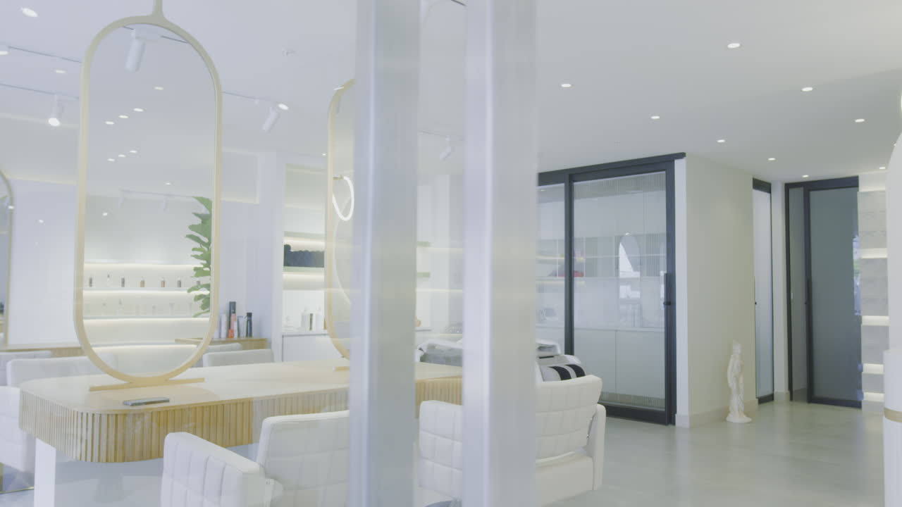 A soft panning shot of a modern spa and beauty center. The space is decorated in white, with sleek mirrors and contemporary furniture.